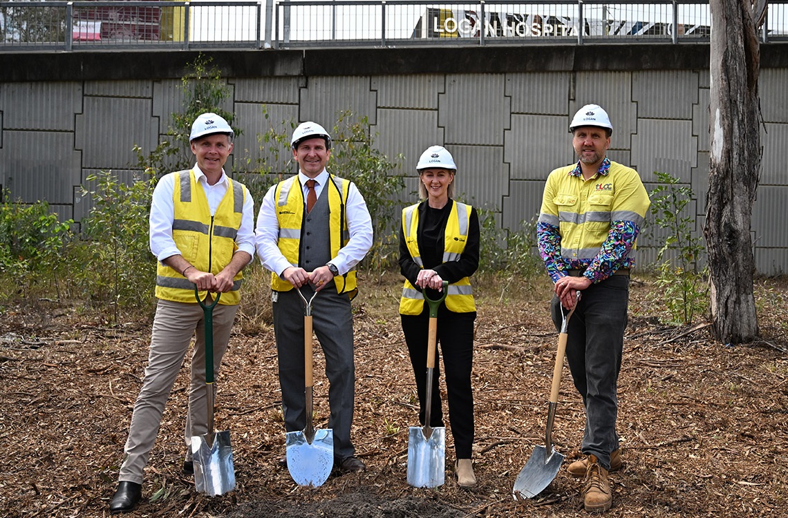 Four officials wearing hard hats and safety vests all holding shovels resting on the dirt