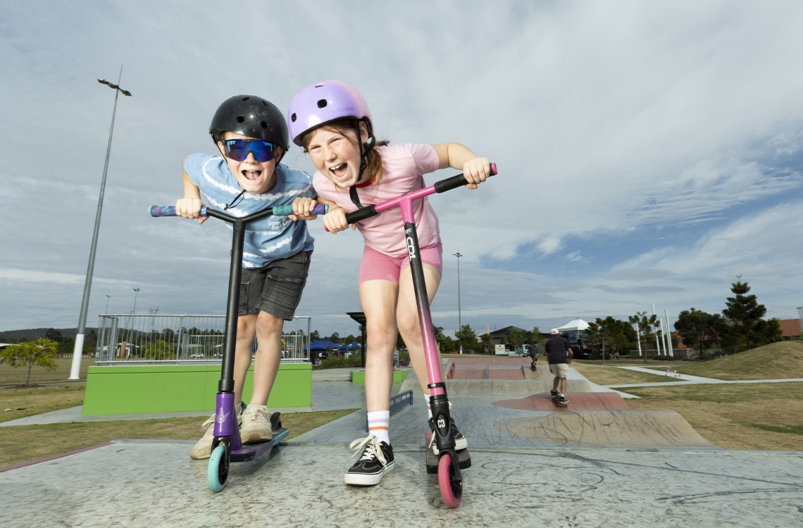 Boy and girl with scooters at a skate park
