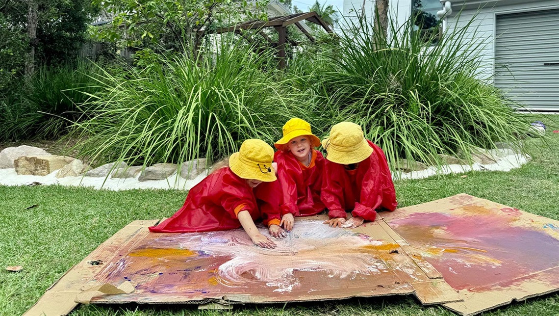 Group of children painting a board on the grass