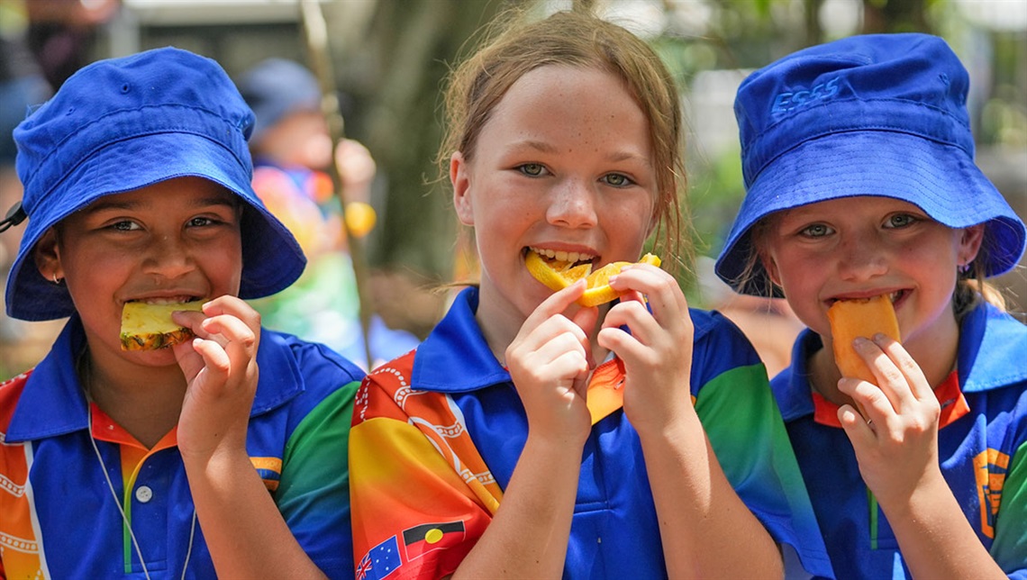 Two boys and a girl smiling and eating fruit