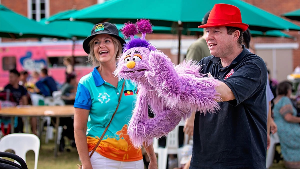 A man performing with a purple puppet and a lady smiling and laughing