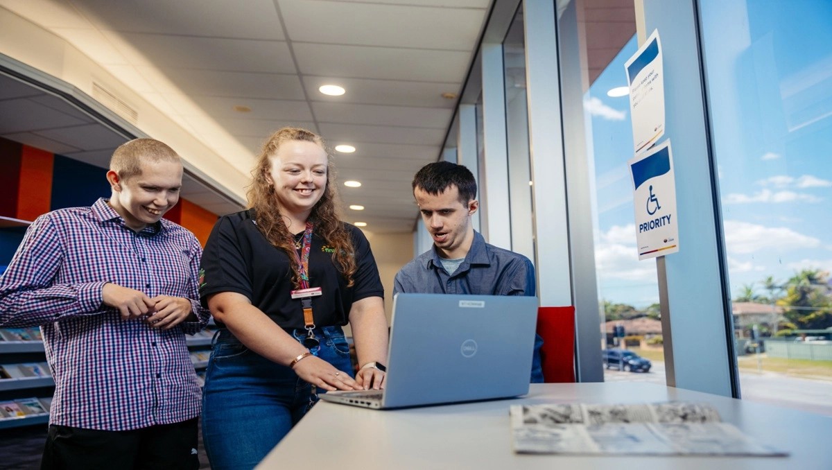 Disabled customers stand with a Library officer using a laptop