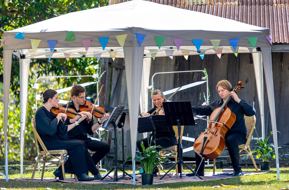 A string quartet sitting and playing their instruments under a marquee in the garden at Mayes Cottage
