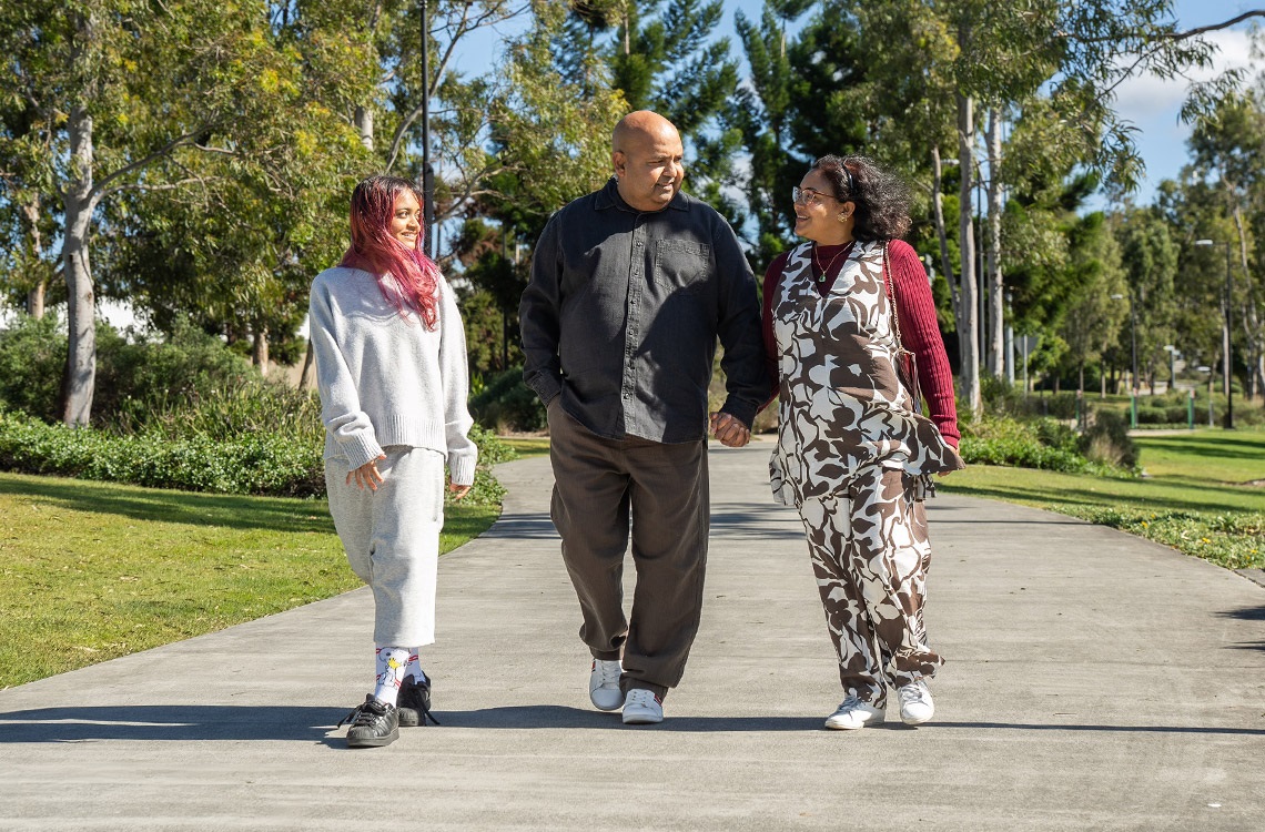 Mother, father and teenage daughter walking happily on a pathway through the park