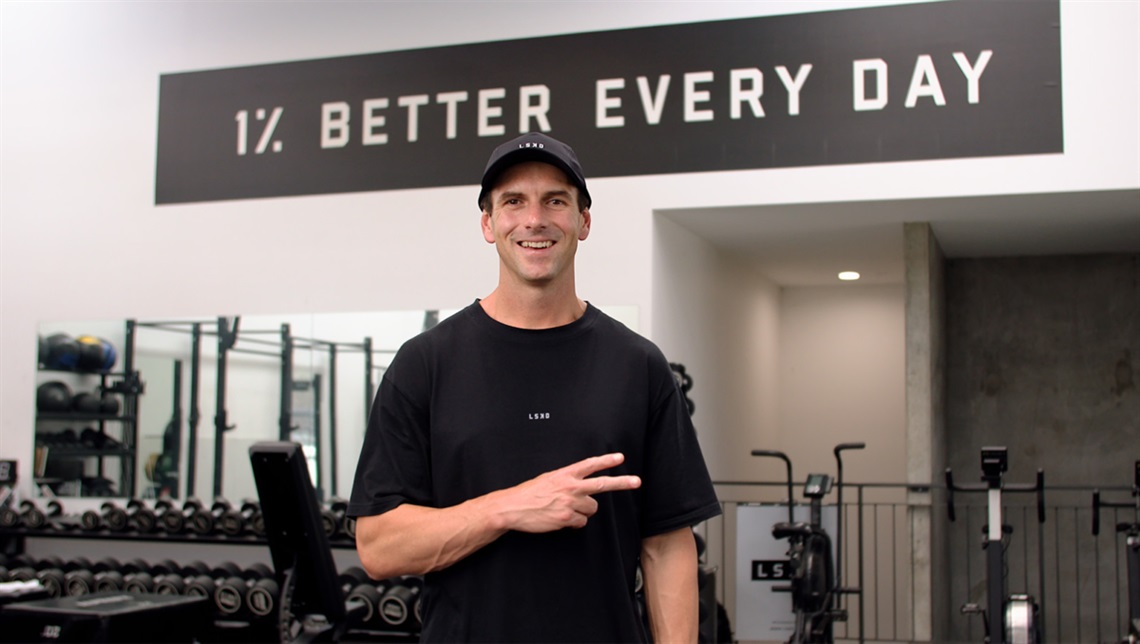 Jason Daniel standing in front of a sign saying 1% better every day