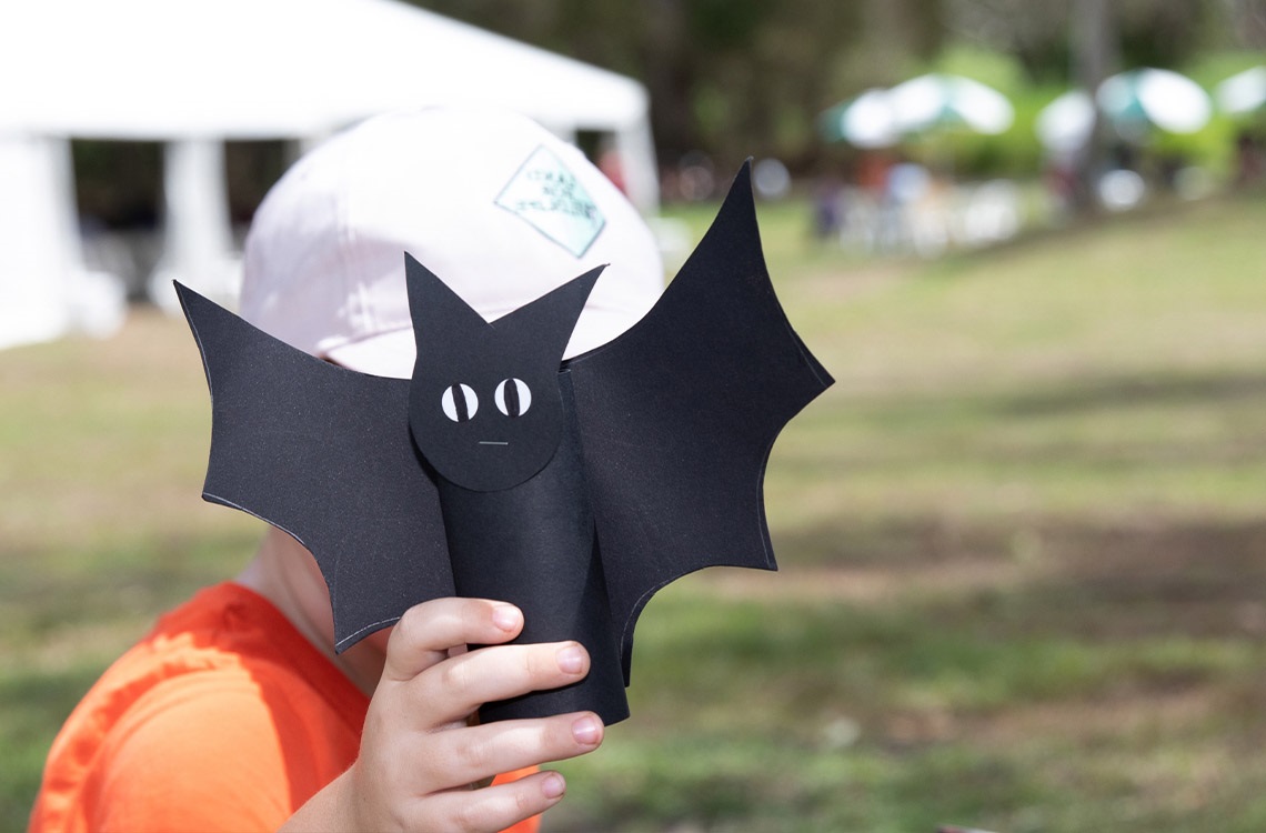 Child holding a craft bat made from cardboard in front of their face